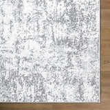 Close-up of Alviva Area Rug with a contemporary gray, charcoal, and white abstract pattern on a wood floor. Corner