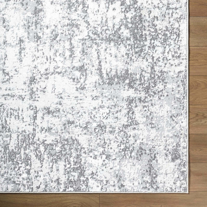 Close-up of Alviva Area Rug with a contemporary gray, charcoal, and white abstract pattern on a wood floor. Corner