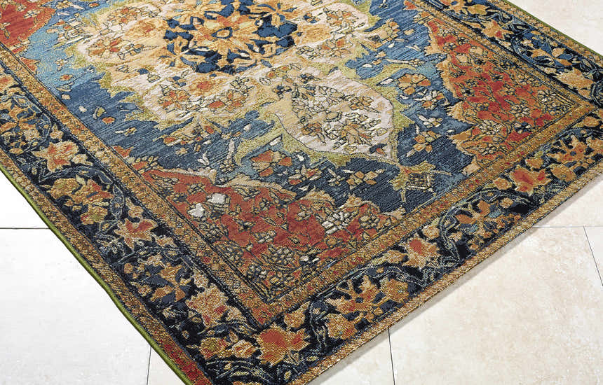 Close-up of Zorea Traditional Area Rug featuring floral pattern in blue, gold, and rust on a beige tile floor. Corner