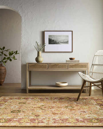 Entryway scene with a traditional Alusia Area Rug in peach, gold and green tones. Console table and woven chair. Roomscene-Rectangle