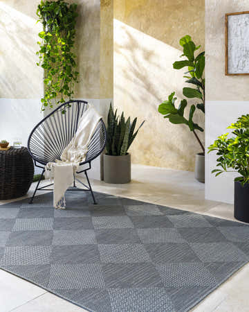 Contemporary patio scene with gray checkered Aulani Area Rug, modern chair, and potted plants. Roomscene-Rectangle