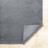 Close-up of the gray Aulani Area Rug showing its woven texture and geometric diamond pattern on a tiled floor. Fold