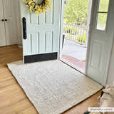 Entryway scene with Ambel Cream Jute Rug on wood floor, light blue door with yellow wreath, and view to front porch. Roomscene-Rectangle