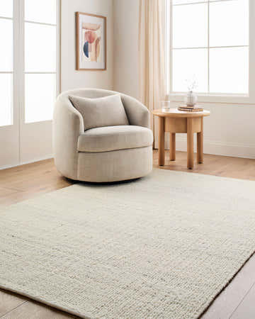 Neutral living room with Padoo Ivory Solid Hand Woven Wool Area Rug, beige chair, wood floors, and natural light. Roomscene-Rectangle