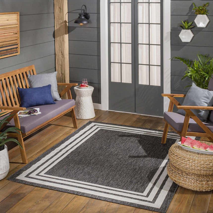 Outdoor patio scene with Coonamble Bordered Antrasit Rug, wood furniture, gray walls, and plants. Modern farmhouse style. Roomscene-Square