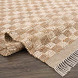 Close-up of the hand-woven Ionut Checkered Jute Area Rug. Beige and tan checkerboard pattern with jute texture and fringe. Fold