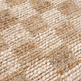 Close-up of the hand woven Ionut Checkered Jute Area Rug. Beige and tan jute fibers create a textured, checkered pattern. Texture