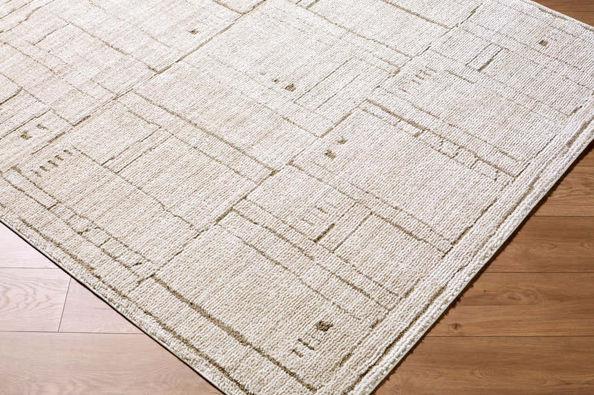 Close-up of Alma Machine Woven Elle Decor x LIVABLISS EDAL-2300 Area Rug. Taupe rug with a geometric pattern on wood floor. Corner