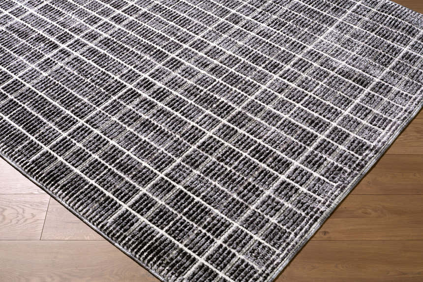Close-up of Odeon Elle Decor x LIVABLISS EDOD-2302 rug. Black, charcoal, and cream geometric grid pattern on wood floor. Corner