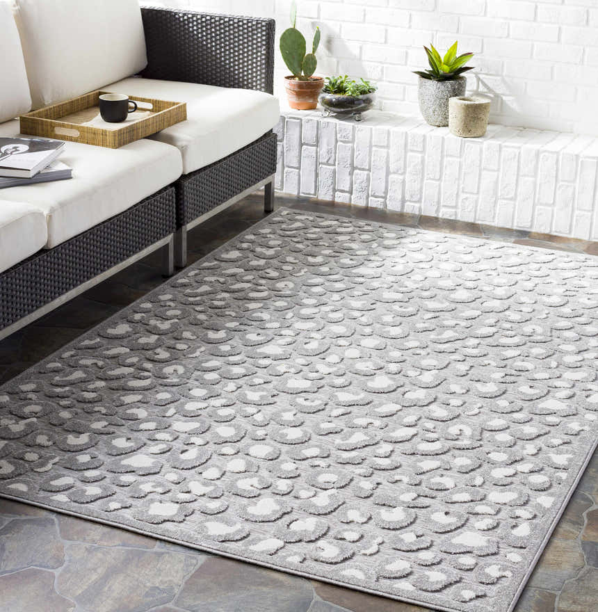 Living room scene with a gray and white animal print Greensborough Performance Rug, black wicker sofa, and white brick wall. Roomscene-Rectangle