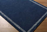 Close up of the hand-tufted Tufape Modern Minimalist Area Rug. Navy blue wool with a striped border. Contemporary style. Corner