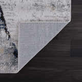 Close-up of the Fremantle Gray Marble Rug showing its cream, gray, gold, and blue abstract pattern and woven backing. Fold