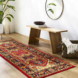 Entryway with a red, orange, and black bohemian Malpas Area Rug, wood bench, round mirror, and potted plant. Roomscene-Runner