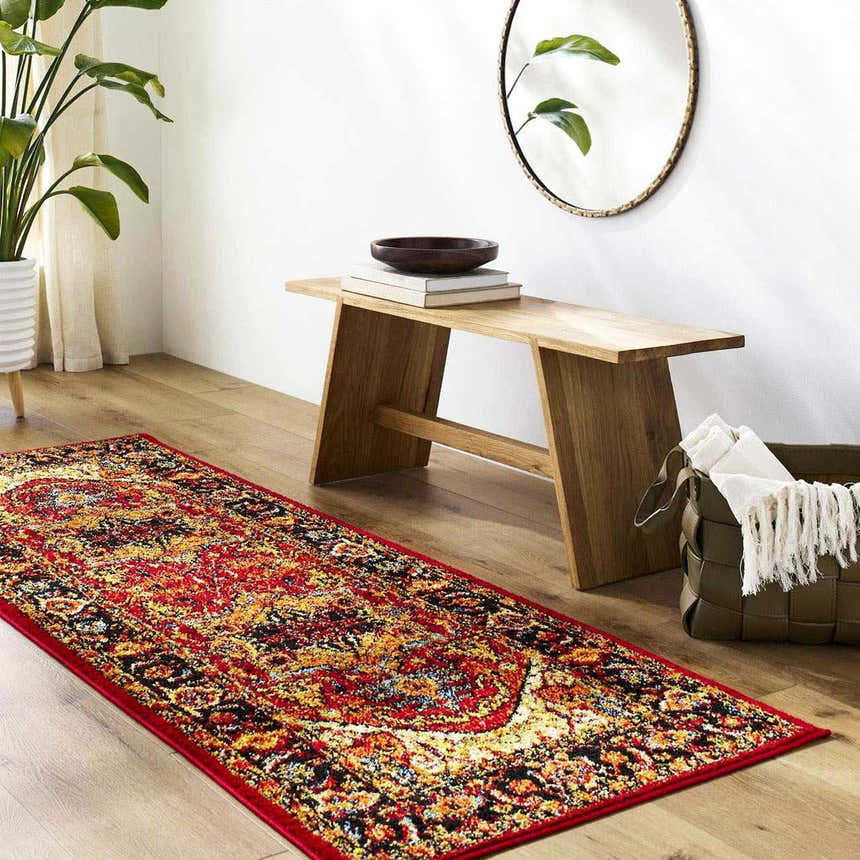 Entryway with a red, orange, and black bohemian Malpas Area Rug, wood bench, round mirror, and potted plant. Roomscene-Runner