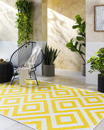 Sunlit patio with a yellow and white geometric Maven Area Rug, chair, and plants. Roomscene-Rectangle