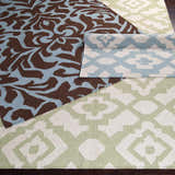 Close-up of Oppelo Area Rug showing dark brown and sage geometric patterns, hand woven wool texture. Styleshot