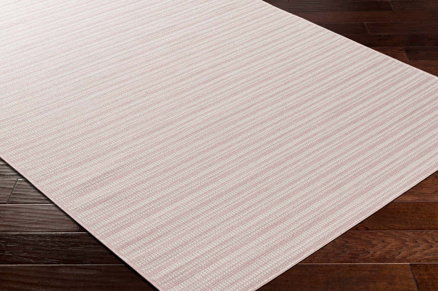 Close-up of the Greg Pink Area Rug showing its striped pattern and soft pink and cream colors on dark wood flooring. Corner