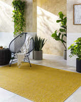 Bright mustard Nuela rug in a sunlit indoor patio with plants and modern chair. Roomscene-Rectangle