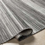 Close-up of the Kris Black Area Rug showing the beachhouse and dark gray woven texture and rolled edge. Fold