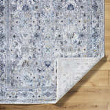 Close-up of the Irida Area Rug showing a traditional floral pattern in dark gray, denim, and light gray on a wood floor. Fold