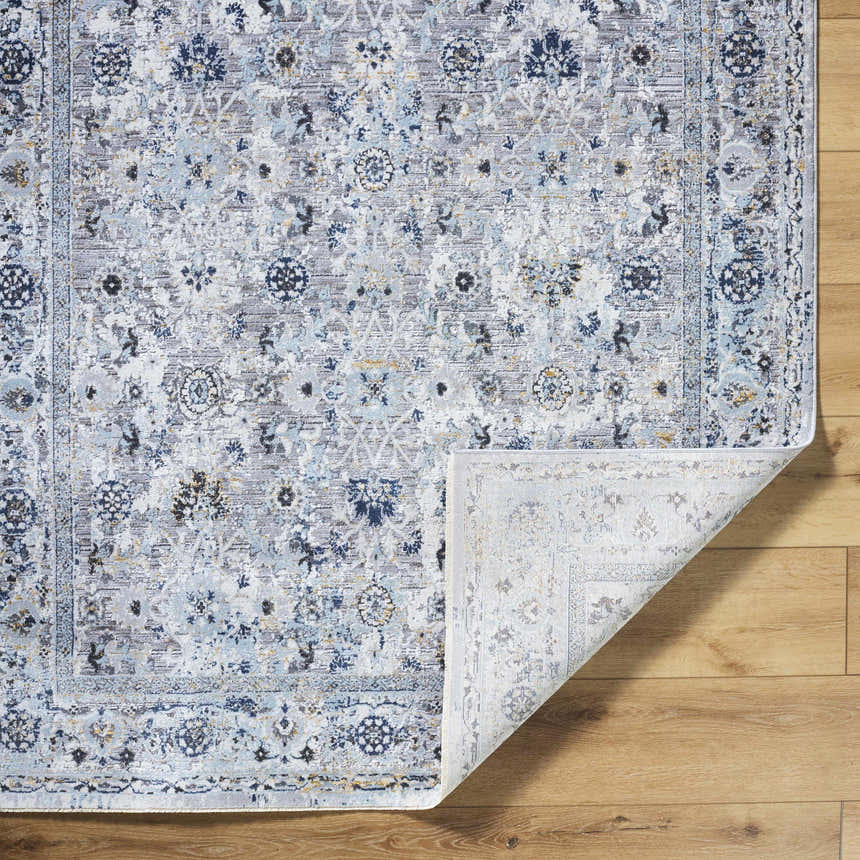 Close-up of the Irida Area Rug showing a traditional floral pattern in dark gray, denim, and light gray on a wood floor. Fold