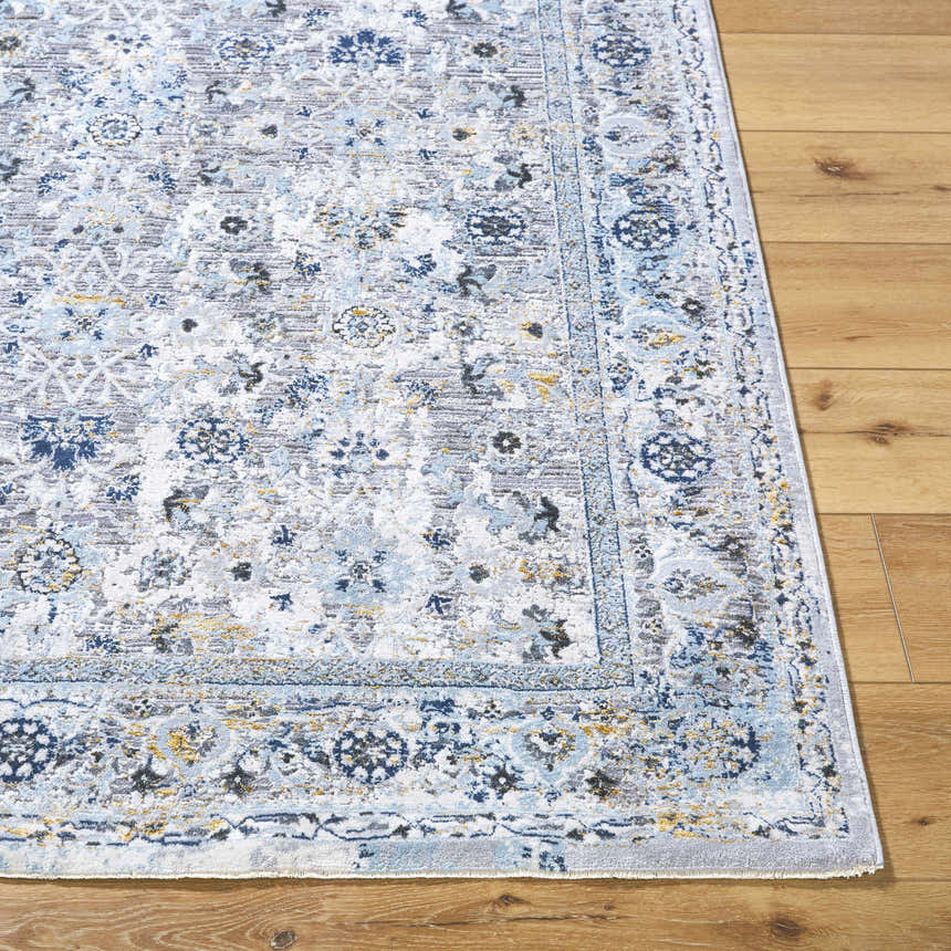 Close-up of the Irida Area Rug showing its traditional floral pattern in denim, gray, and nutmeg on a wood floor. Front