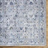 Close-up of the Irida Area Rug showing its denim, gray, and nutmeg floral pattern and machine-woven texture. Corner
