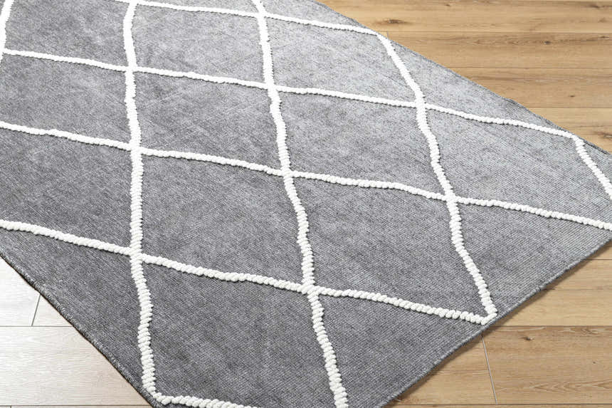 Close-up of the Amani Gray Washable Rug with a white geometric diamond pattern on light wood flooring. Corner