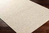 Close-up of the Alyra Beige Solid Area Rug showing its woven texture and neutral color on dark wood flooring. Corner