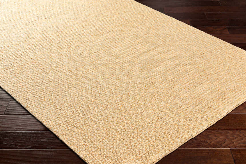 Close-up of the hand-woven Alyra Yellow Solid Area Rug showing texture and color on a dark wood floor. Corner