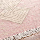 Close-up of the hand-woven Sang Area Rug. Features a geometric pattern in dusty pink, mauve, and tan with fringe detail. Texture