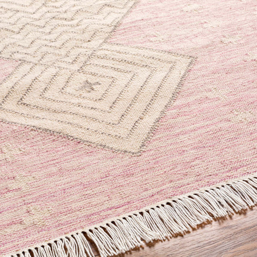 Close-up of the hand-woven Sang Area Rug. Features a geometric pattern in dusty pink, mauve, and tan with fringe detail. Texture