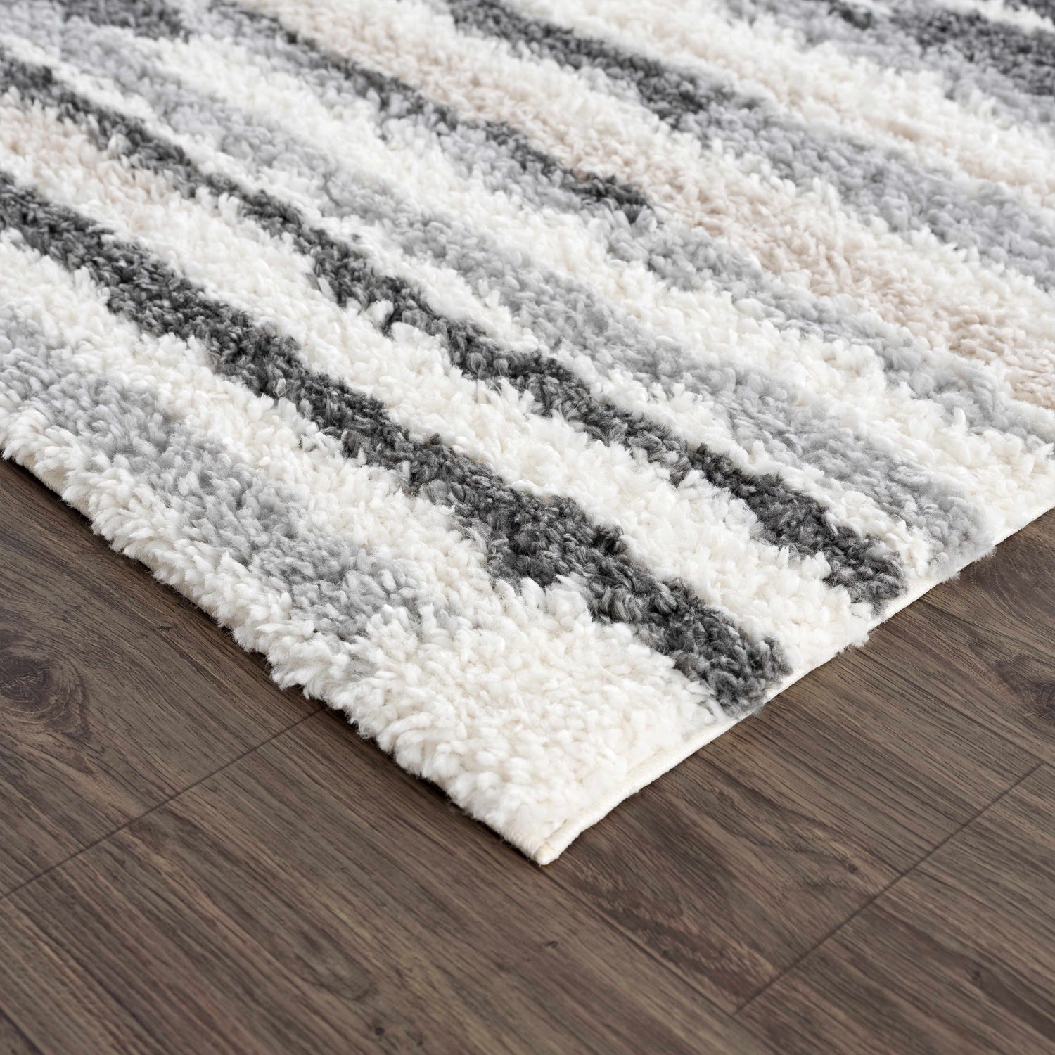 Close up of the Zoya Irregular Striped Area Rug showing the beige, cream, and gray shag stripes and texture. Corner