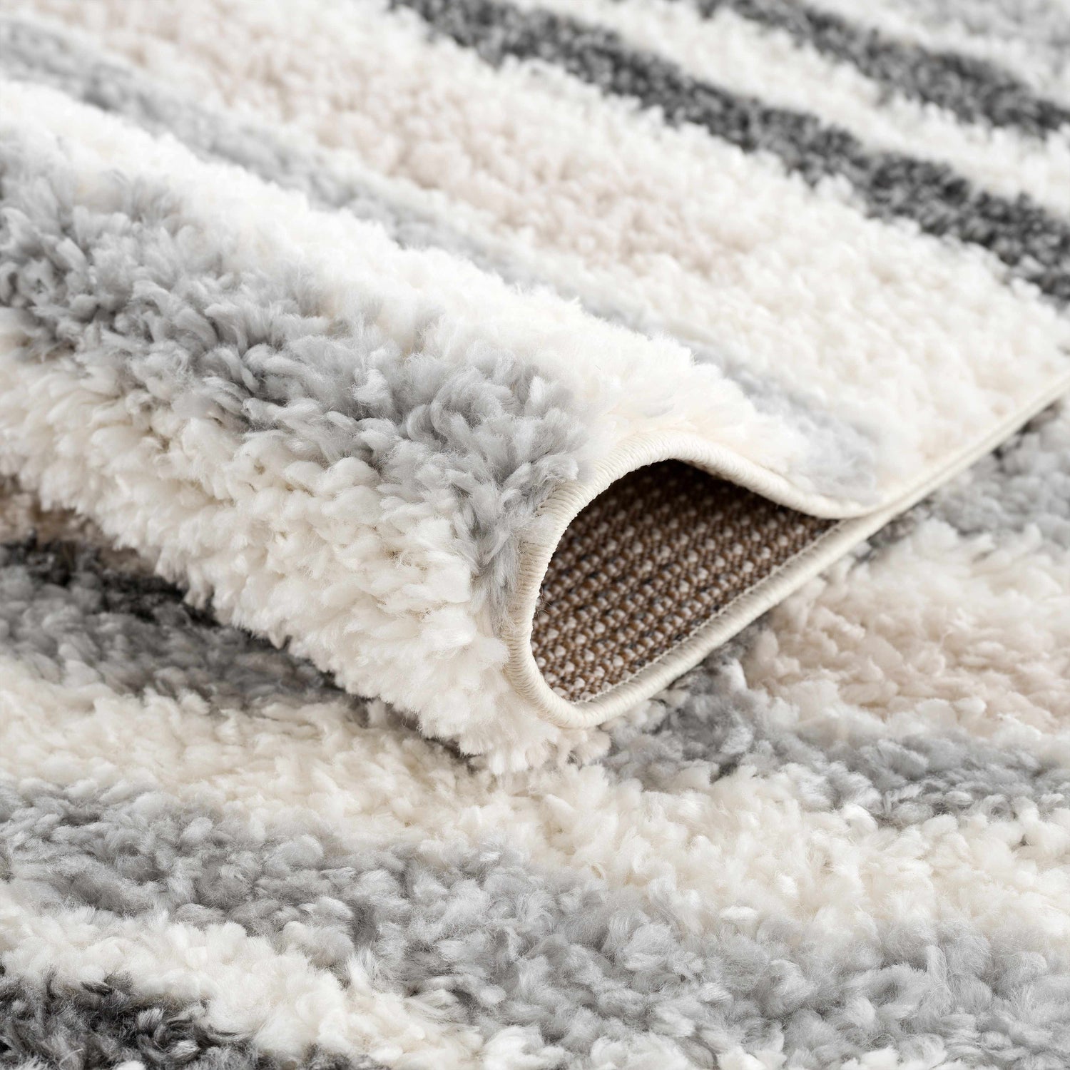 Close-up of the plush Zoya Irregular Striped Area Rug, showing its soft texture and beige, cream, and gray stripes. Fold