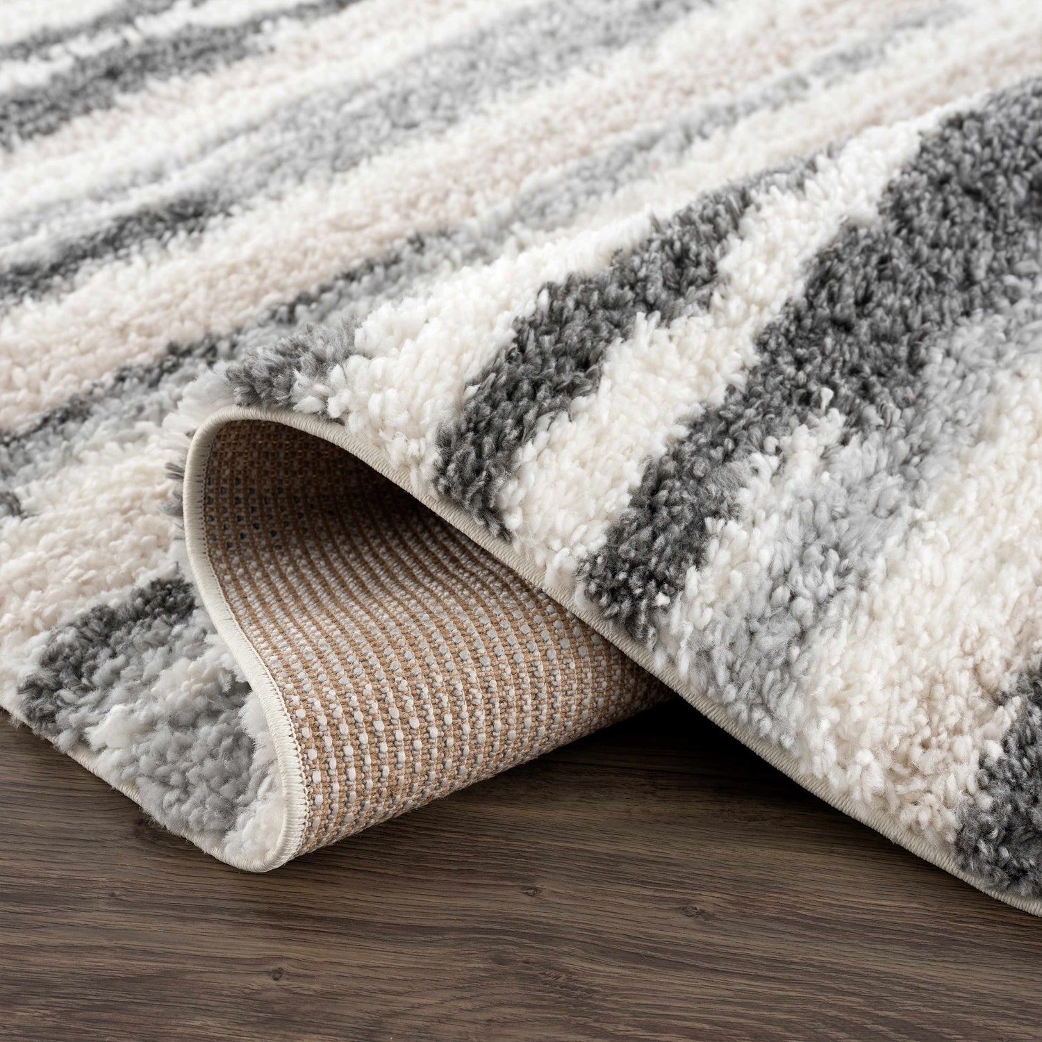 Close-up of the plush Zoya Irregular Striped Area Rug. Beige, cream, and gray shag stripes with a machine-woven backing. Fold