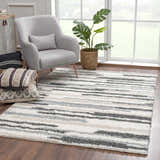 Living room scene with a gray chair and the Zoya Irregular Striped Area Rug in beige, cream, and gray. Roomscene-Rectangle