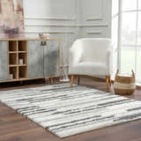 Living room scene with a Zoya Irregular Striped Area Rug, cream sherpa chair, and wood cabinet. Modern, neutral tones. Roomscene-Rectangle