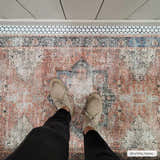 Person standing on Rosman Distressed Washable Area Rug in a bathroom with beige, black, and brick red colors. Styleshot