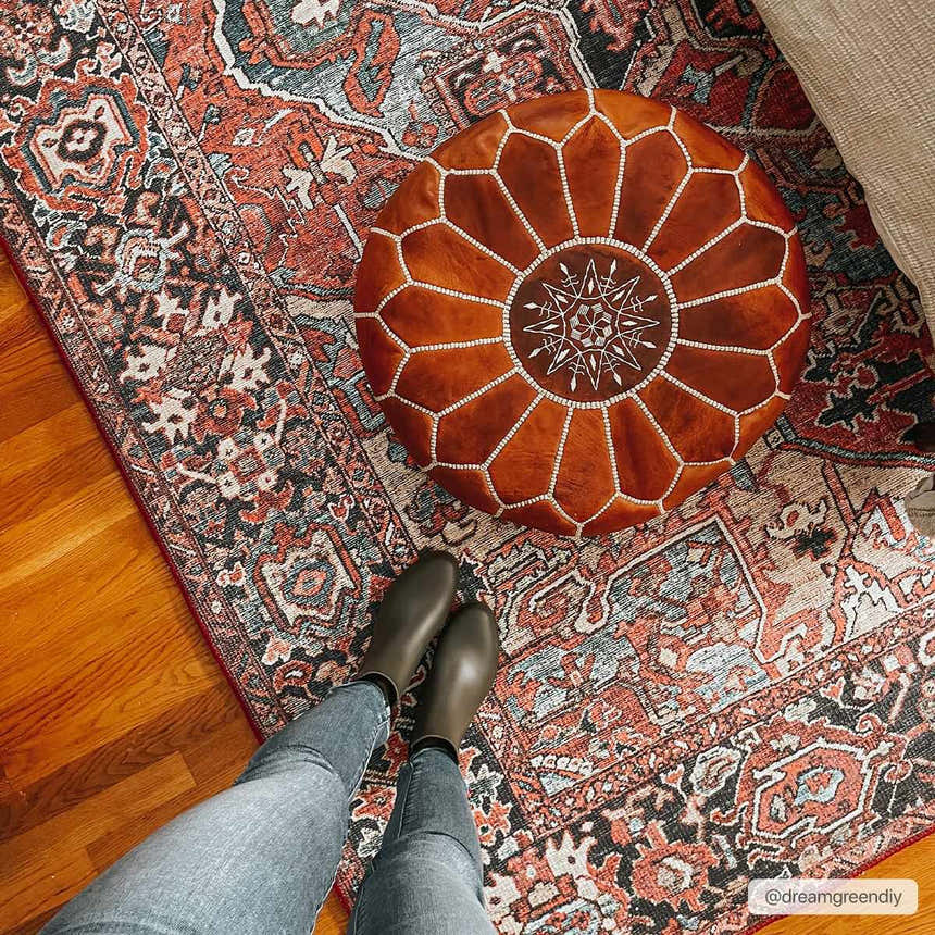 Bohemian Neyland Area Rug styled with a leather pouf on a wood floor. Red, navy, and beige tones. Styleshot