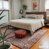Bedroom scene with a red and navy Neyland Area Rug, beige bedding, and a brown leather pouf. Roomscene-Rectangle