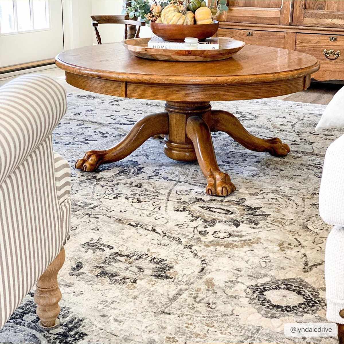 Living room scene with a round wood table on a Georgiana Area Rug. The rug has beige, black, and gray tones. Styleshot