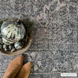 Close-up of Greenpoint Dusty Blue Washable Rug with a beige, black, and sage pattern. Styled with Christmas ornaments and brown boots. Styleshot