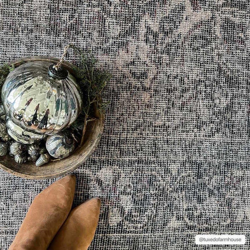 Close-up of Greenpoint Dusty Blue Washable Rug with a beige, black, and sage pattern. Styled with Christmas ornaments and brown boots. Styleshot