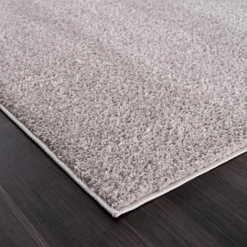Close-up of the Judy Solid Gray Washable Shag Rug showing its plush texture and light gray color on dark wood floor. Corner