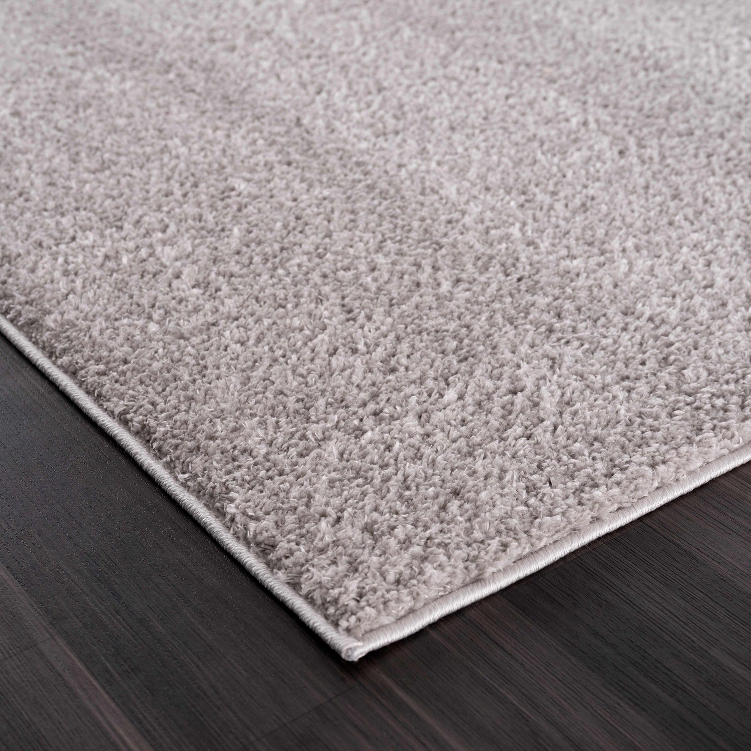 Close-up of the Judy Solid Gray Washable Shag Rug showing its plush texture and light gray color on dark wood floor. Corner