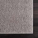 Close-up of the Judy Solid Gray Washable Shag Rug showing its soft texture and light gray color on dark wood floor. Swatch