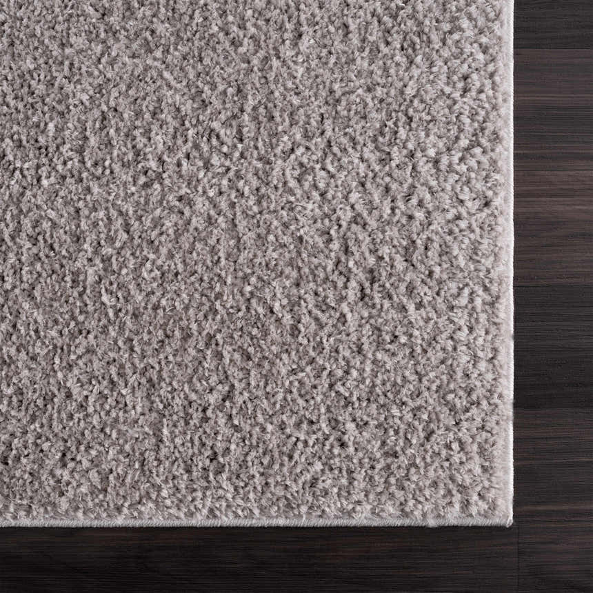 Close-up of the Judy Solid Gray Washable Shag Rug showing its soft texture and light gray color on dark wood floor. Swatch