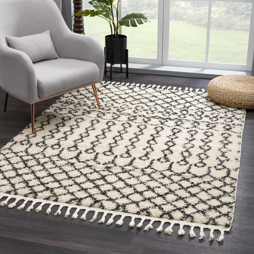 Living room scene with a charcoal and light beige Muni Berber Shag Rug, gray chair, and woven ottoman. Roomscene-Rectangle