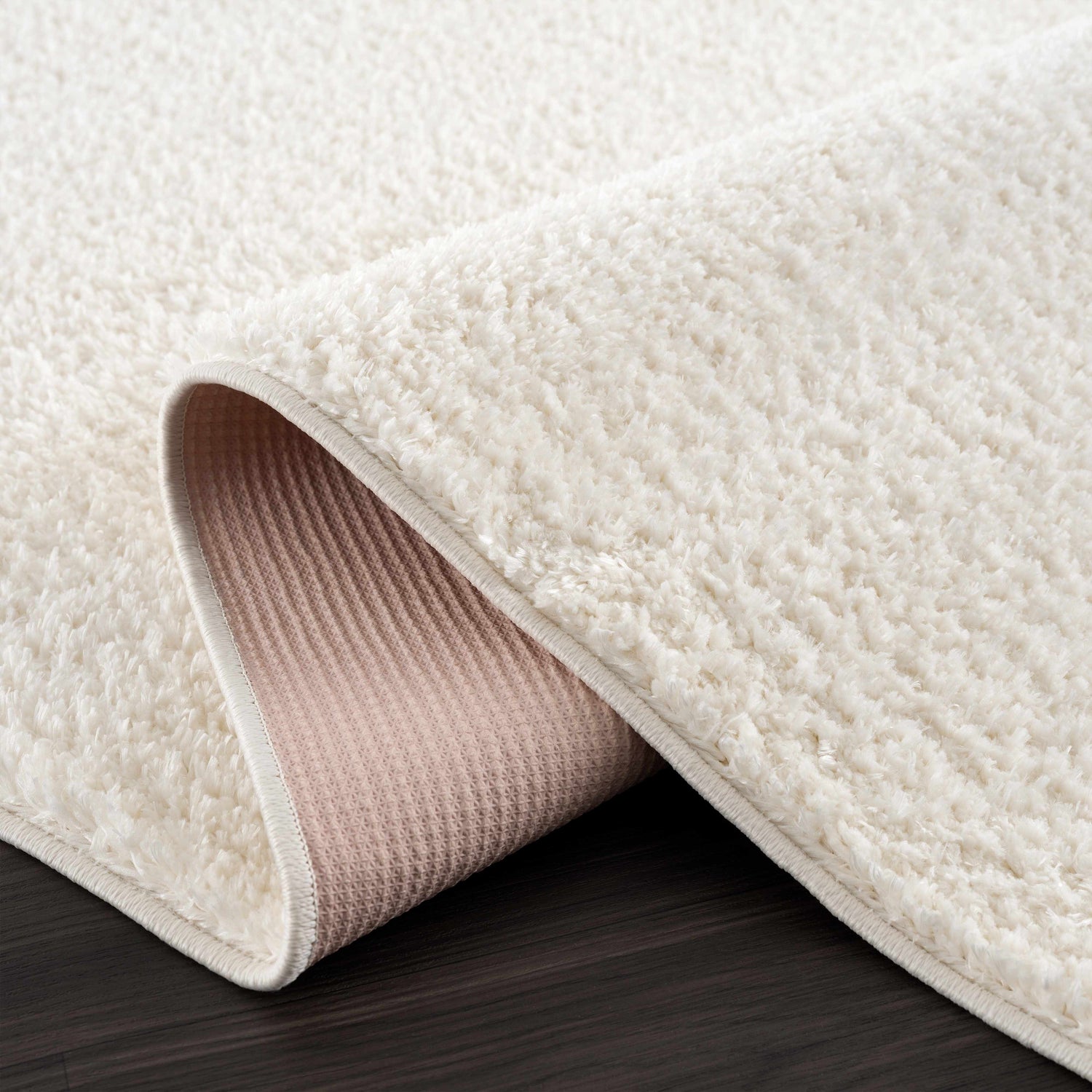 Close-up of the off-white Judy Washable Area Rug, showing its plush shag texture and durable backing on dark wood flooring. Fold