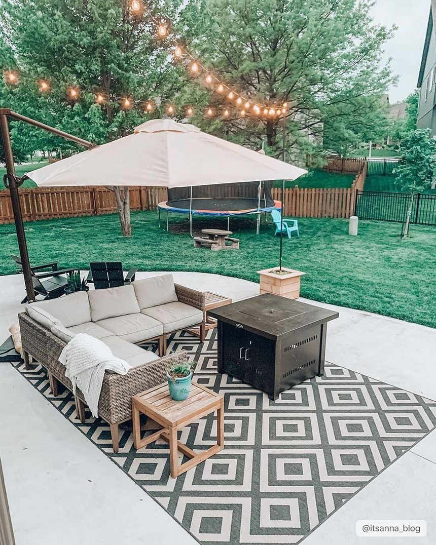 Outdoor patio with Spilsby Geometric rug, wicker sofa, fire pit, and string lights creating a cozy backyard scene. Roomscene-Rectangle